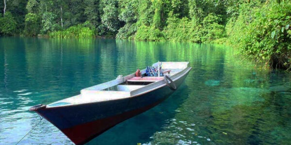 Kejernihan air Danau Labuan Cermin yang memukau, menampilkan refleksi sempurna dari pepohonan hijau di sekitarnya