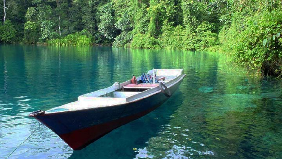 Kejernihan air Danau Labuan Cermin yang memukau, menampilkan refleksi sempurna dari pepohonan hijau di sekitarnya